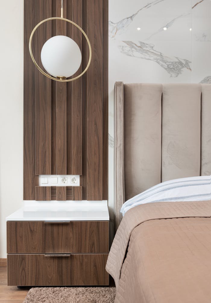 Interior of modern hotel room with bed next to bedside table under lamp hanging from ceiling